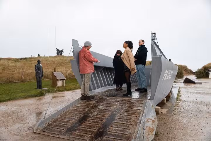 Tourists exploring a WWII landing craft replica at Normandy D-Day beaches memorial site on overcast day