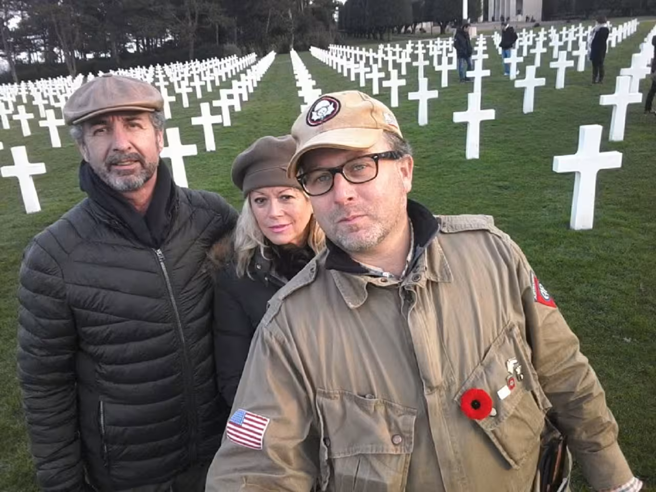 Three visitors posing solemnly among white crosses at Normandy American Cemetery, D-Day memorial, France