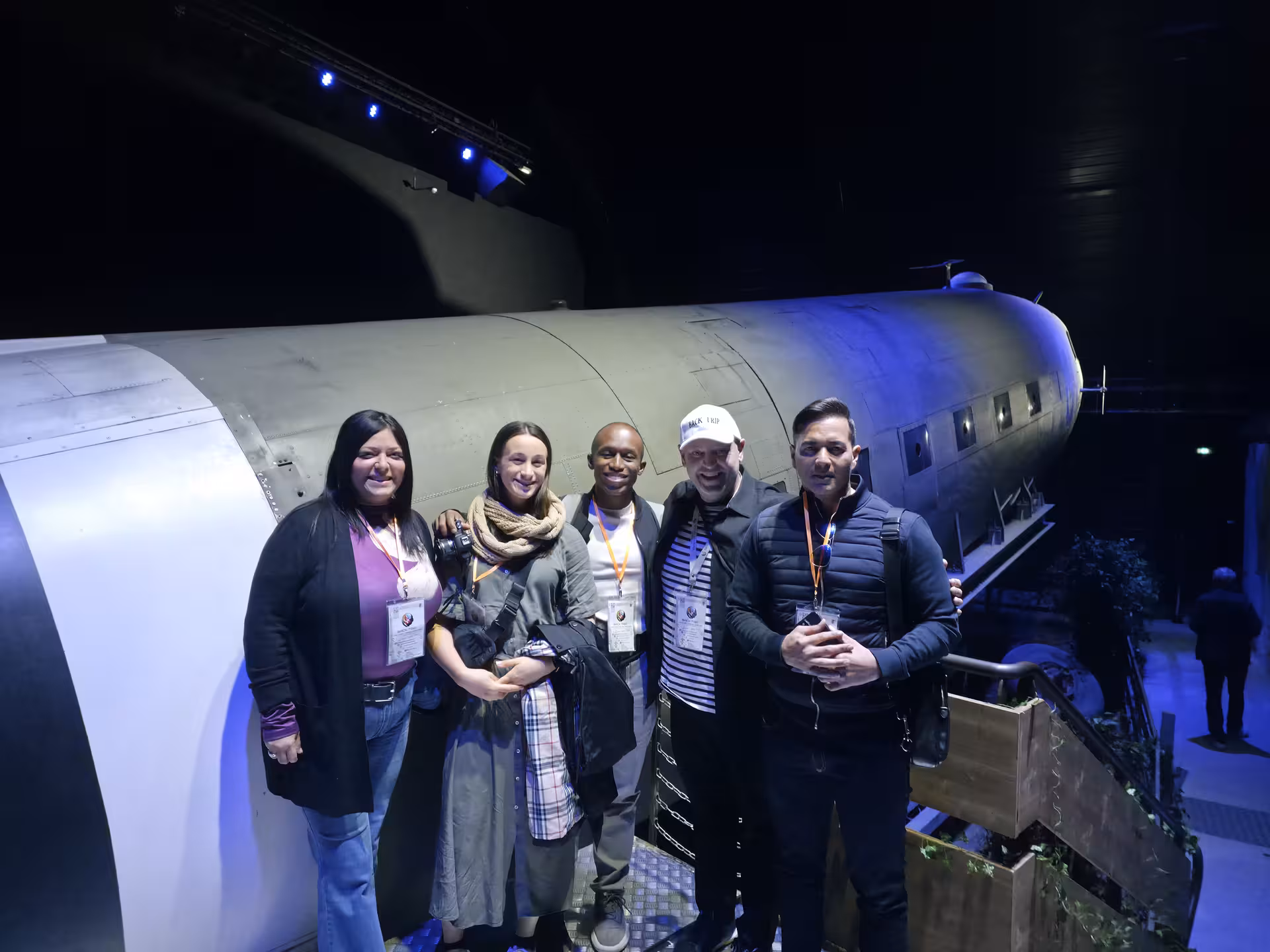 Happy tour group poses beside a historic WWII aircraft display at a Normandy D-Day museum during a private guided tour.