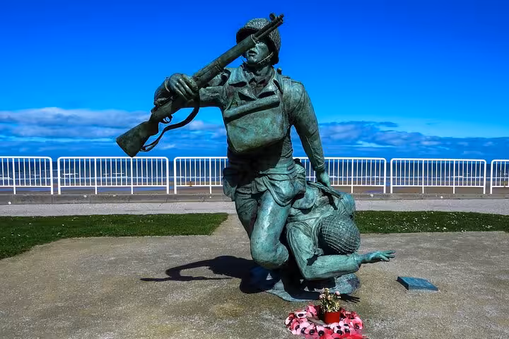 Bronze WWII soldier statue helping fallen comrade at Normandy D-Day memorial with poppy wreaths