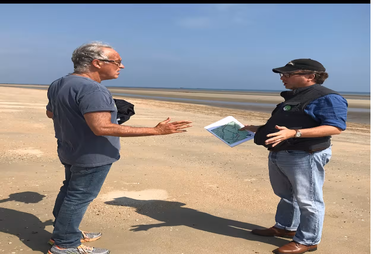 Tour guide holding map discussing Normandy D-Day beaches with visitor on sandy shore