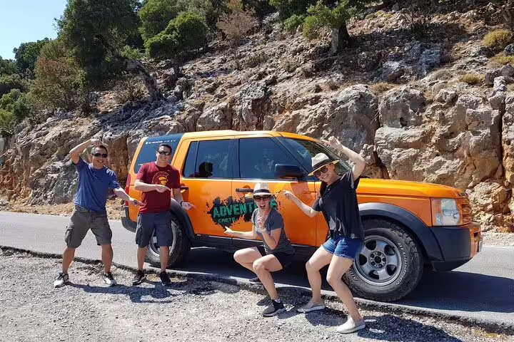Adventurous group posing with an orange jeep during the North Coast Adventure Tour, surrounded by rugged landscapes.