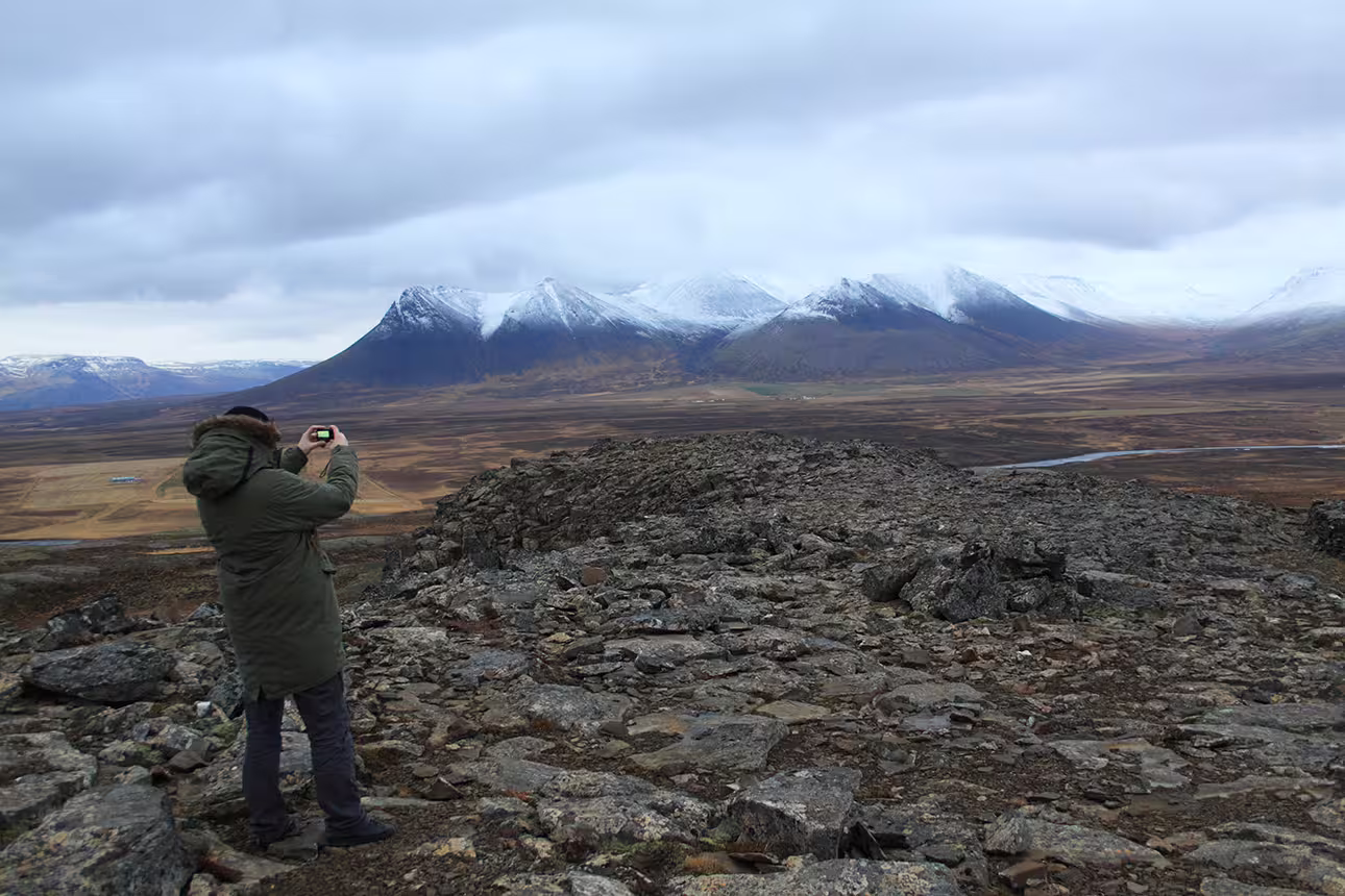 Hiker photographing snow-capped mountains and vast Arctic tundra valley in North Iceland