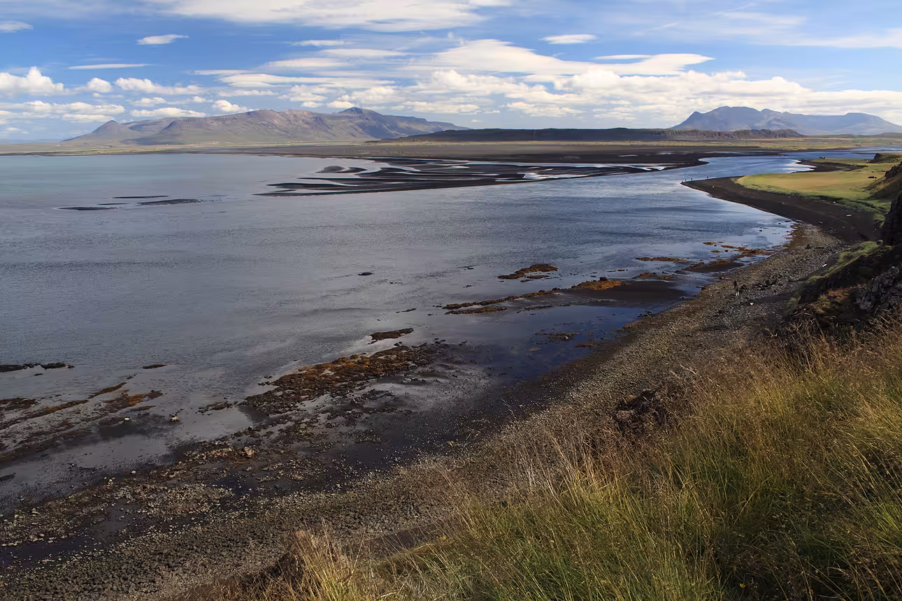 Coastal tidal flats and black sand shores with mountains in North Iceland under a partly cloudy sky
