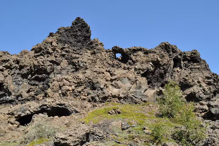 Rugged lava rock formations with a natural arch opening under clear blue skies in North Iceland