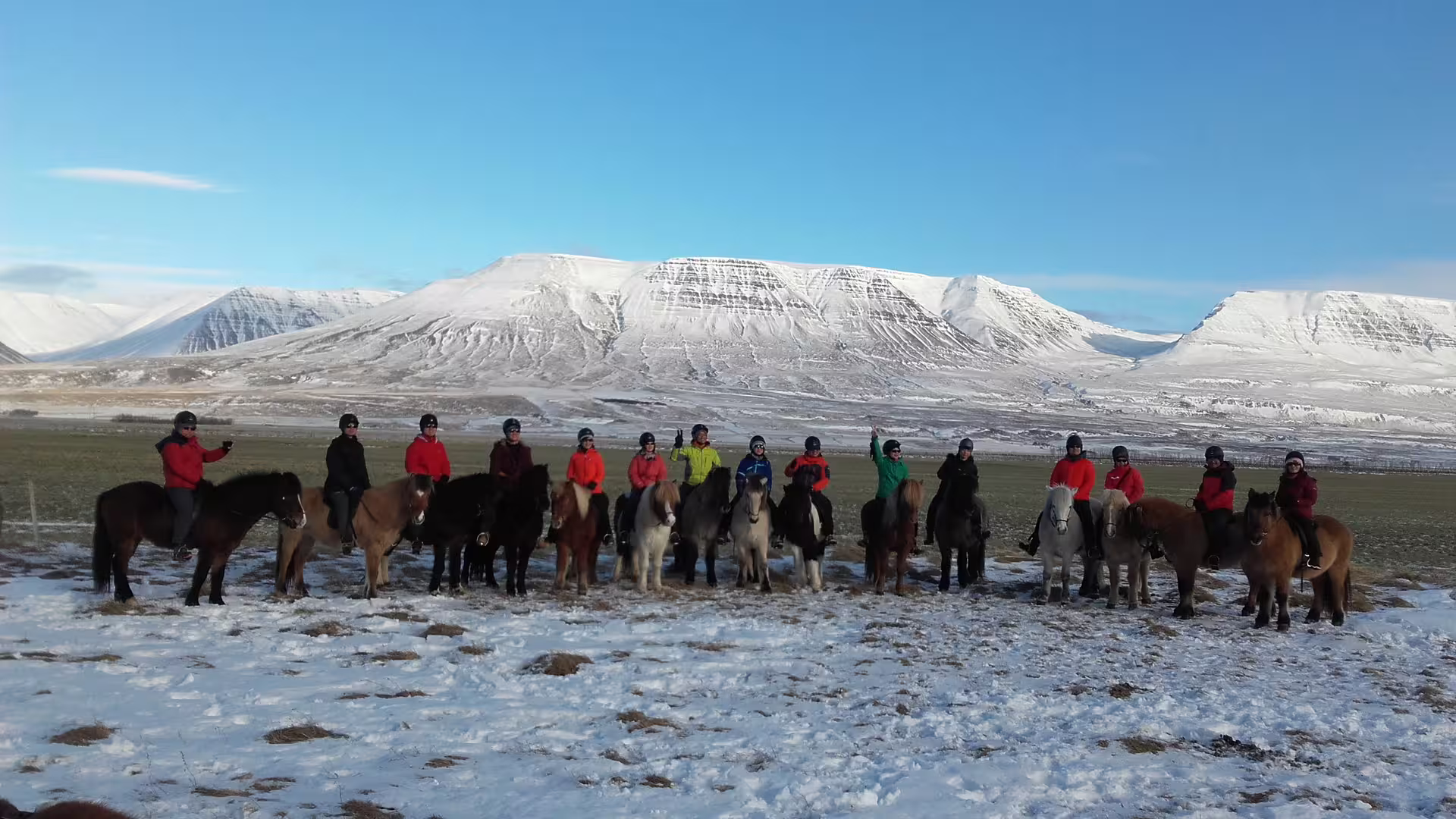 Group of riders on Icelandic horses lined up in snowy landscape with snow-capped mountains in North Iceland