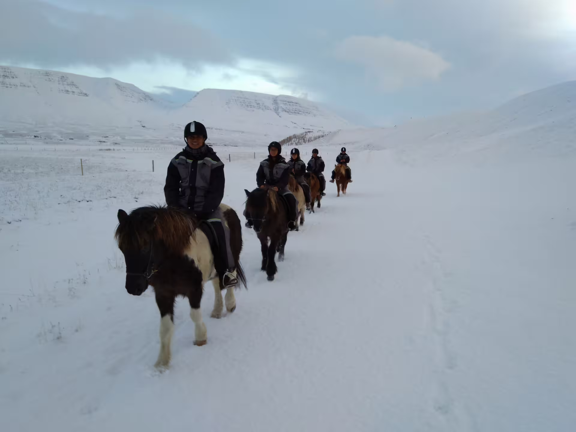 Group of riders on Icelandic horses trekking through snowy landscape with snow-covered mountains in North Iceland