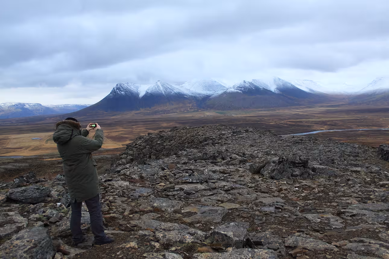Traveler photographing snow-capped mountains and vast valley on private North Iceland tour