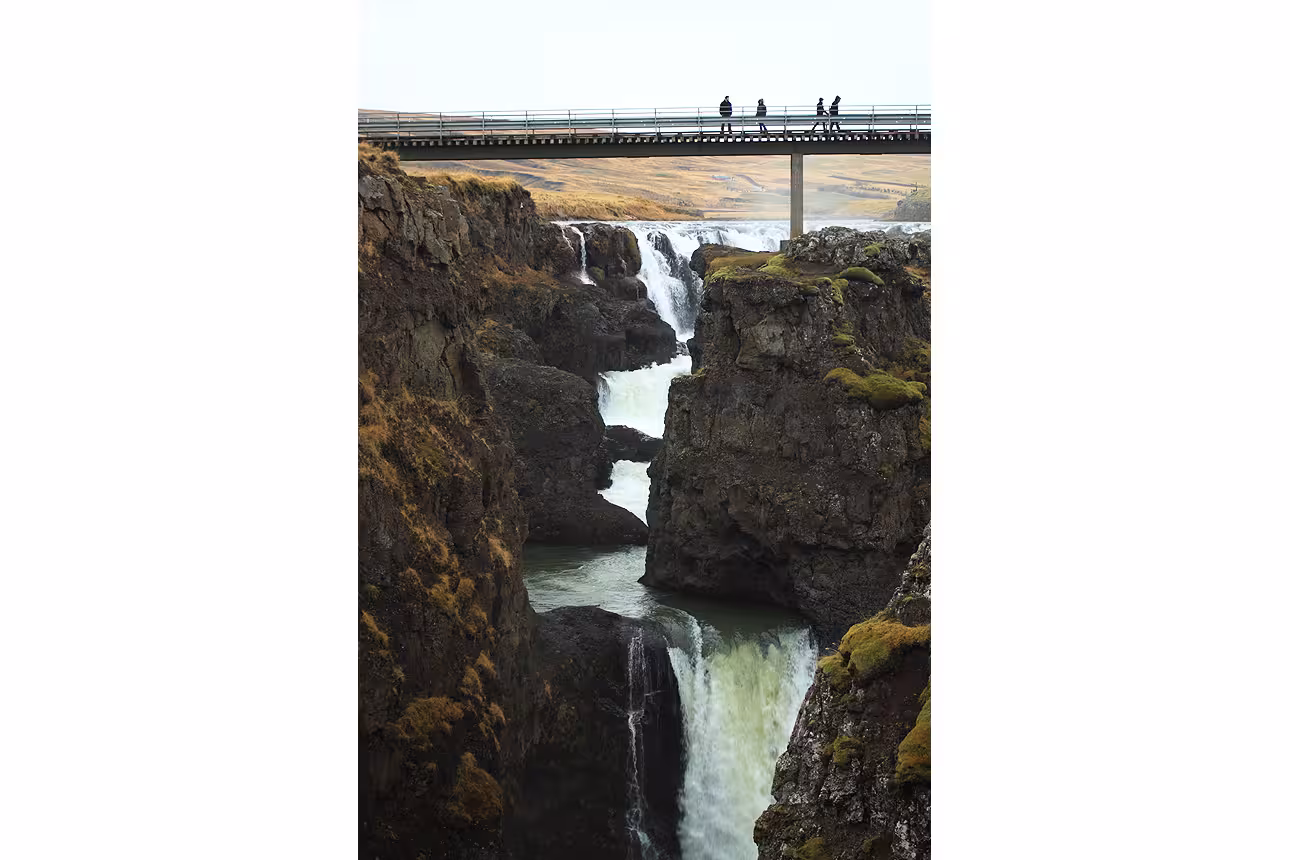 Cascading waterfalls through rocky canyon gorge with tourists on bridge, North Iceland scenic landscape