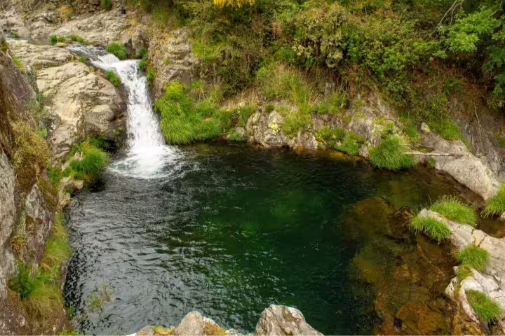Scenic view of a tranquil waterfall and natural pool surrounded by lush greenery in North Portugal, ideal for a self-drive tour.