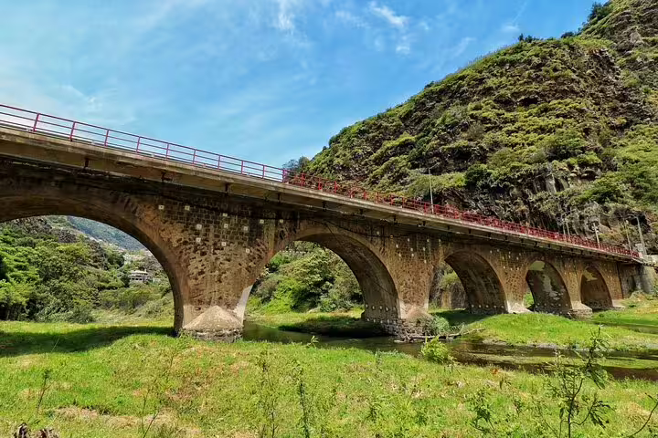 Scenic view of an ancient stone bridge amidst lush green hills on a full day guided tour in Northeast Madeira.