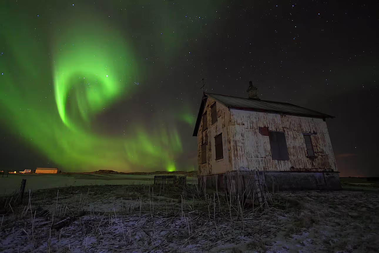 Aurora borealis swirling green northern lights over abandoned white farmhouse in snowy Icelandic landscape