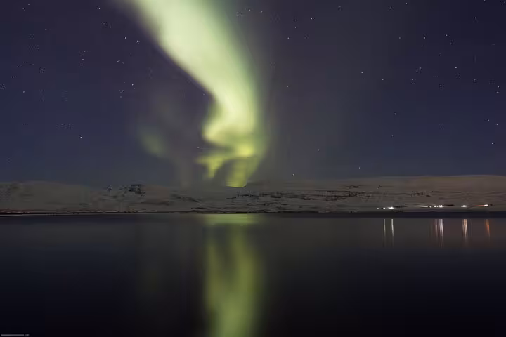 Vibrant green Northern Lights reflecting over a serene lake near Akureyri, Iceland, under a starry night sky.
