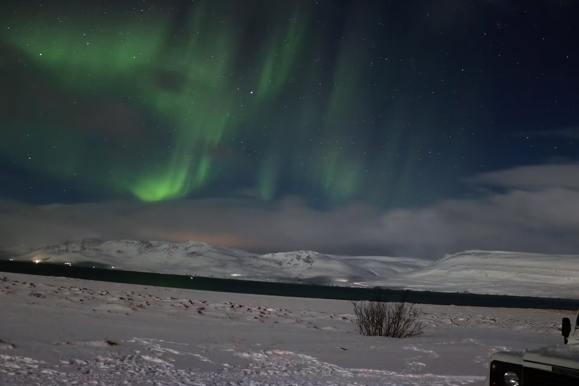 Vivid green northern lights dancing over snow-covered mountains near Akureyri, North Iceland at night