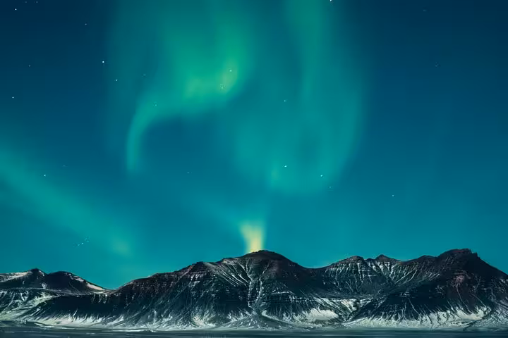 Vibrant green northern lights swirling over snow-capped mountains in the Arctic night sky