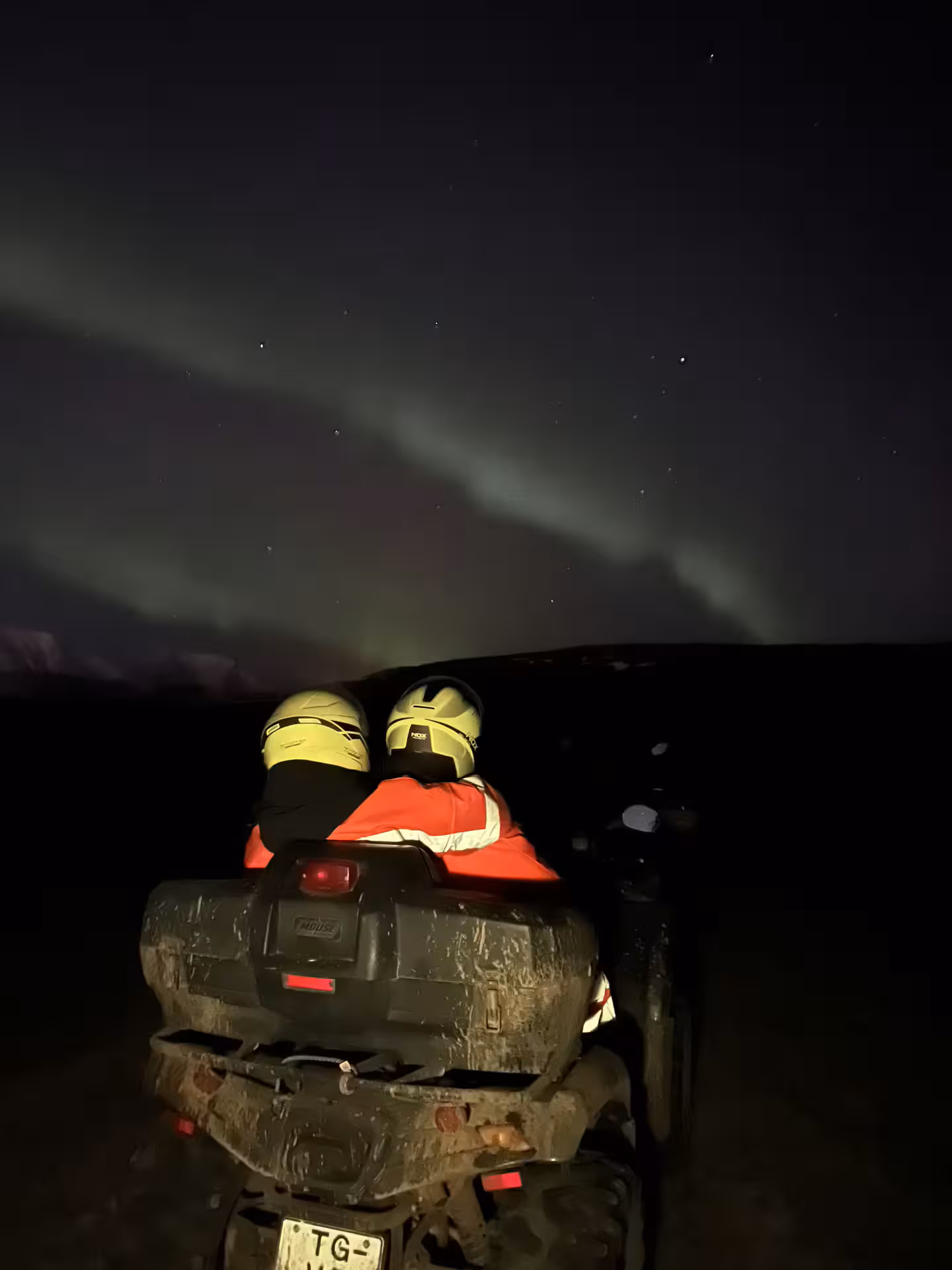 Two yellow helmets on a muddy ATV under the Northern Lights in Iceland at night