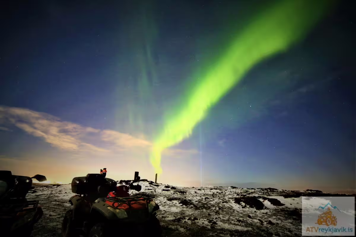 ATV quad bikes parked on snowy terrain under vivid green northern lights in Reykjavik night sky