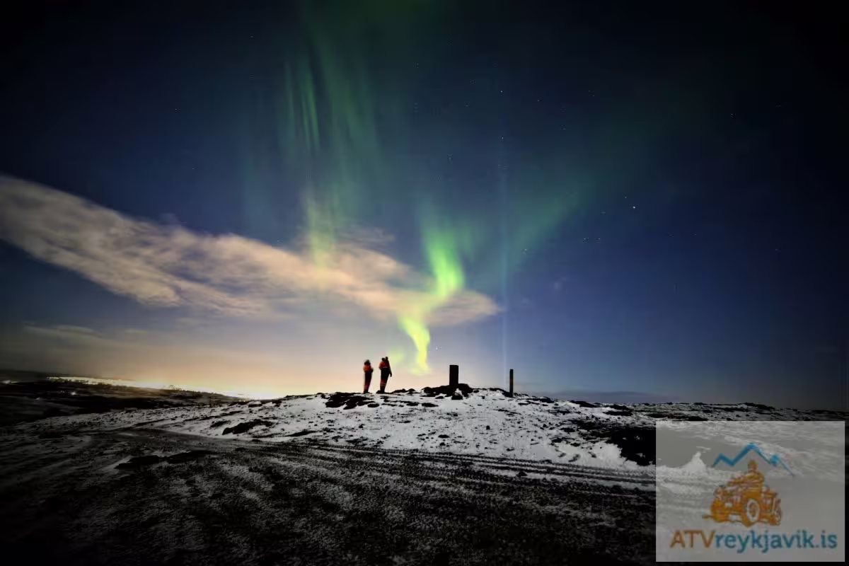 Two people on snowy hilltop watching green northern lights aurora borealis in Reykjavik night sky