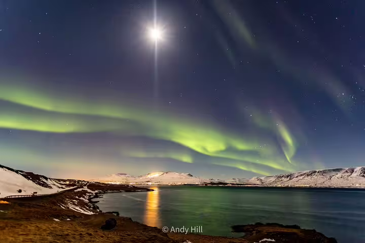 Northern lights dancing over snowy fjord near Akureyri Iceland under bright moonlit sky
