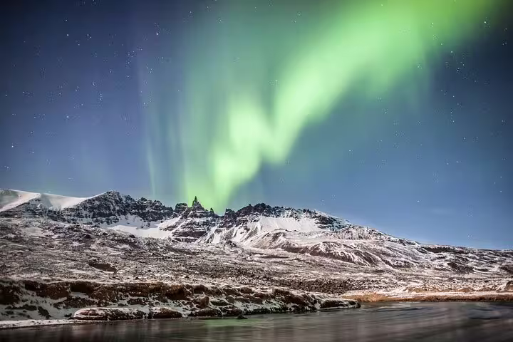 Vivid green northern lights aurora borealis glowing over snow-covered mountains near Akureyri Iceland at night
