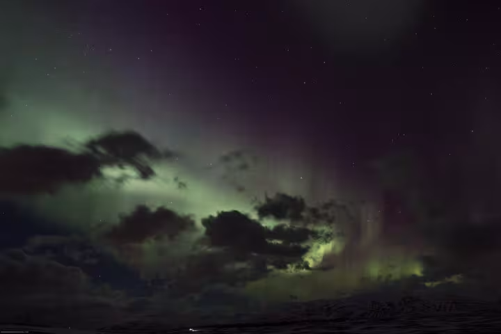 Mystical green auroras dance among clouds in the night sky above Akureyri, Iceland, showcasing nature's beauty.