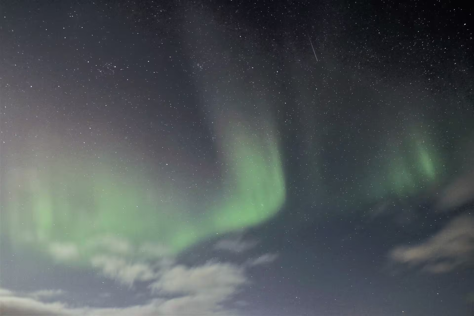 Vibrant green northern lights aurora borealis dancing over starry night sky in North Iceland with clouds below