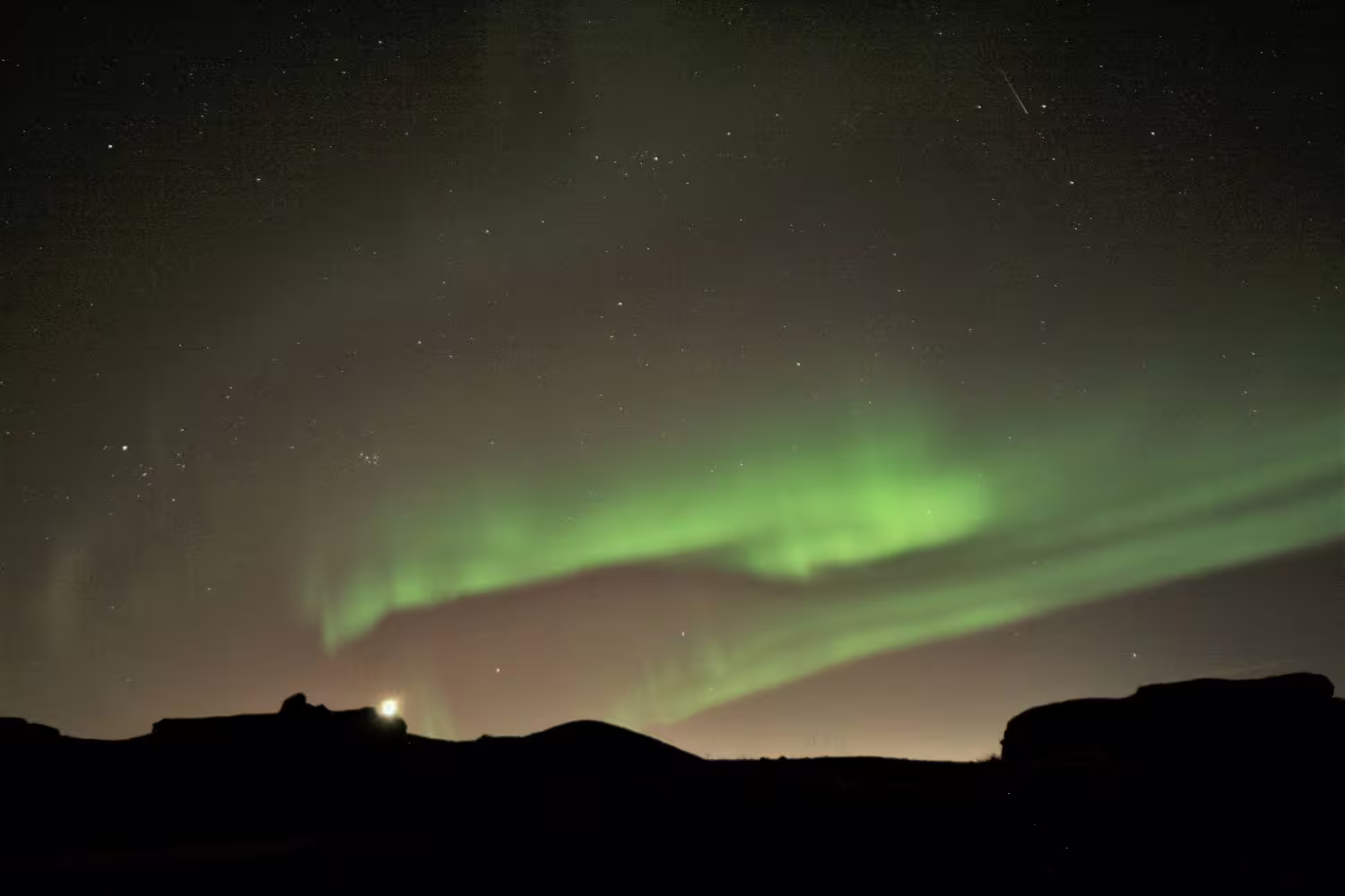 Vivid green northern lights aurora borealis dancing over dark silhouetted hills in Reykjavik Iceland night sky
