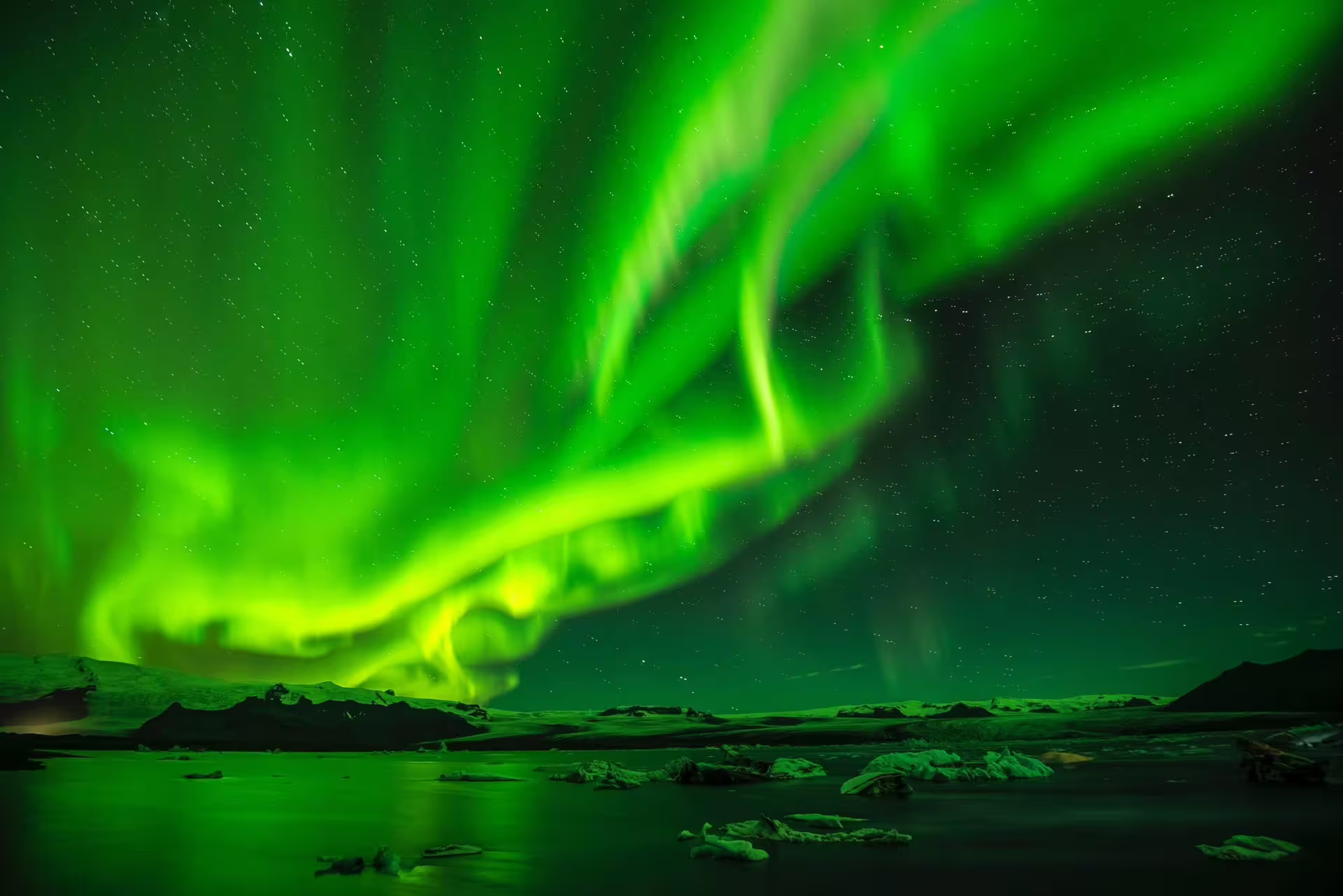 Vivid green aurora borealis swirling over an icy glacial lagoon on a starry night in Iceland