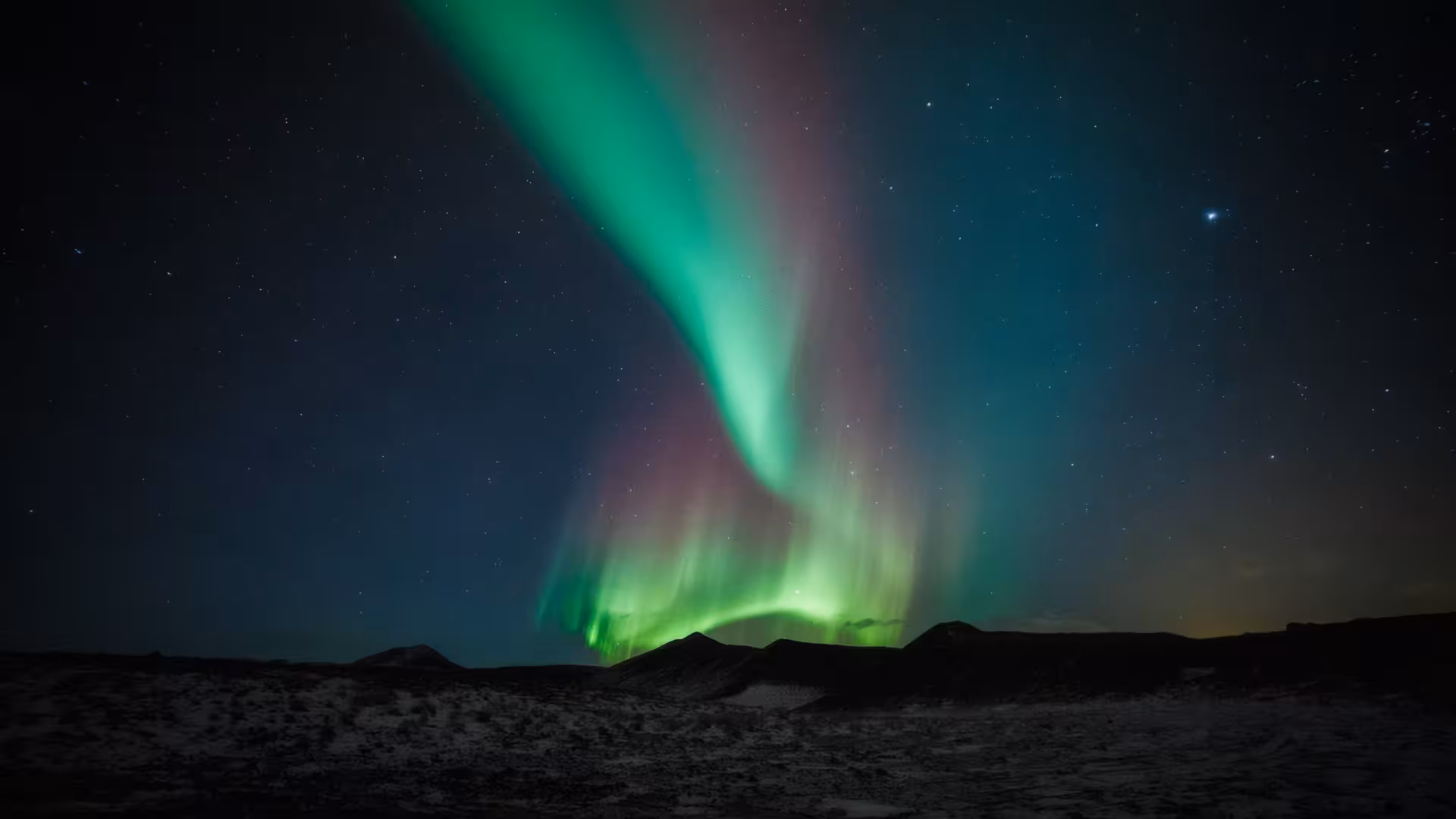 Vibrant green and pink aurora borealis dancing over dark volcanic landscape in Iceland at night