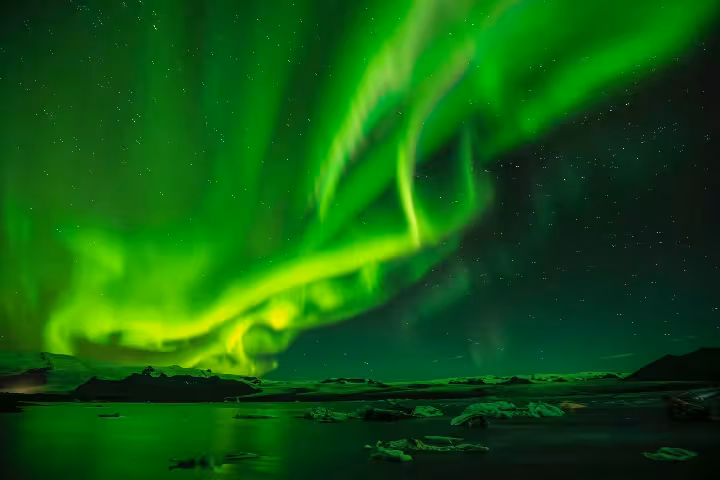 Vibrant green aurora borealis dancing over an icy lagoon under a starry night sky