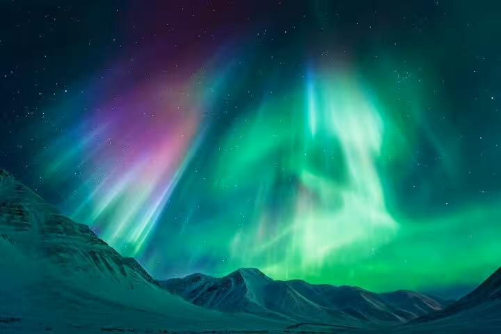 Vivid green and purple northern lights aurora borealis over snow-covered mountains in Iceland night sky