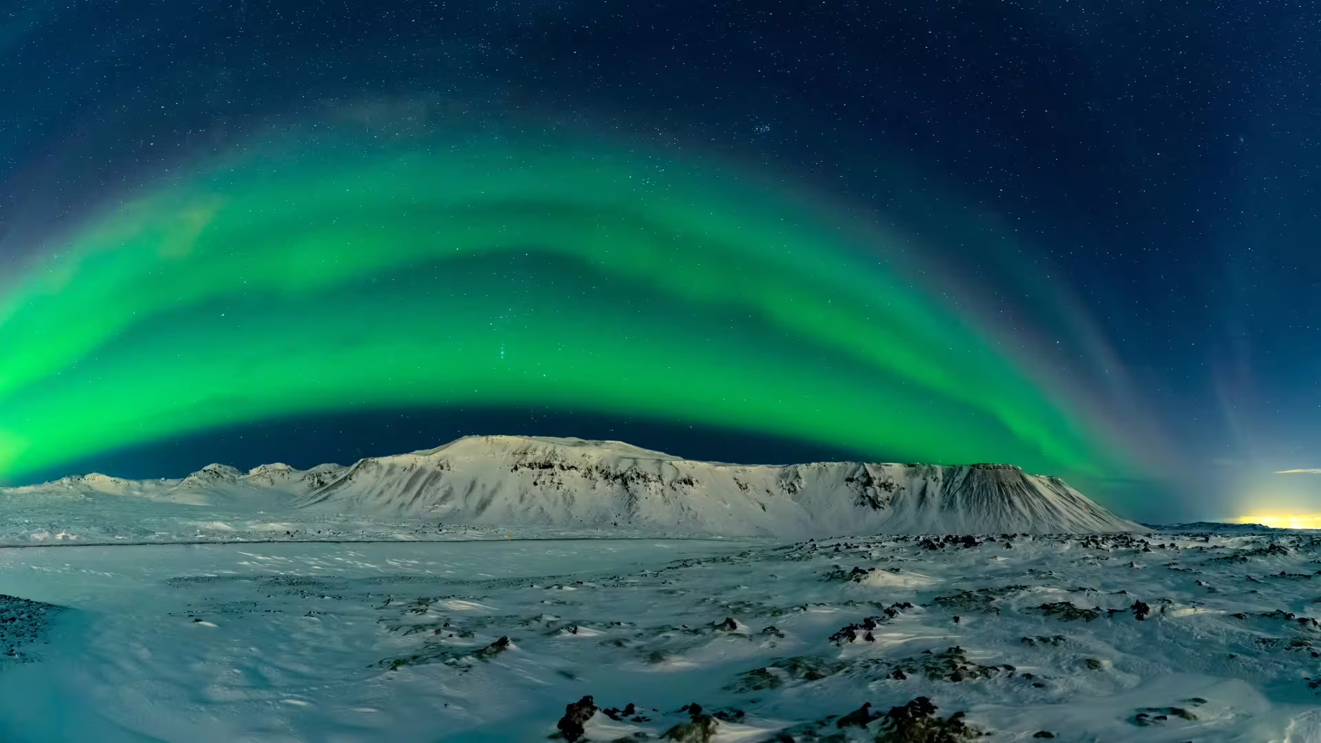 Vibrant green northern lights arching over snow-covered mountains in Iceland at night