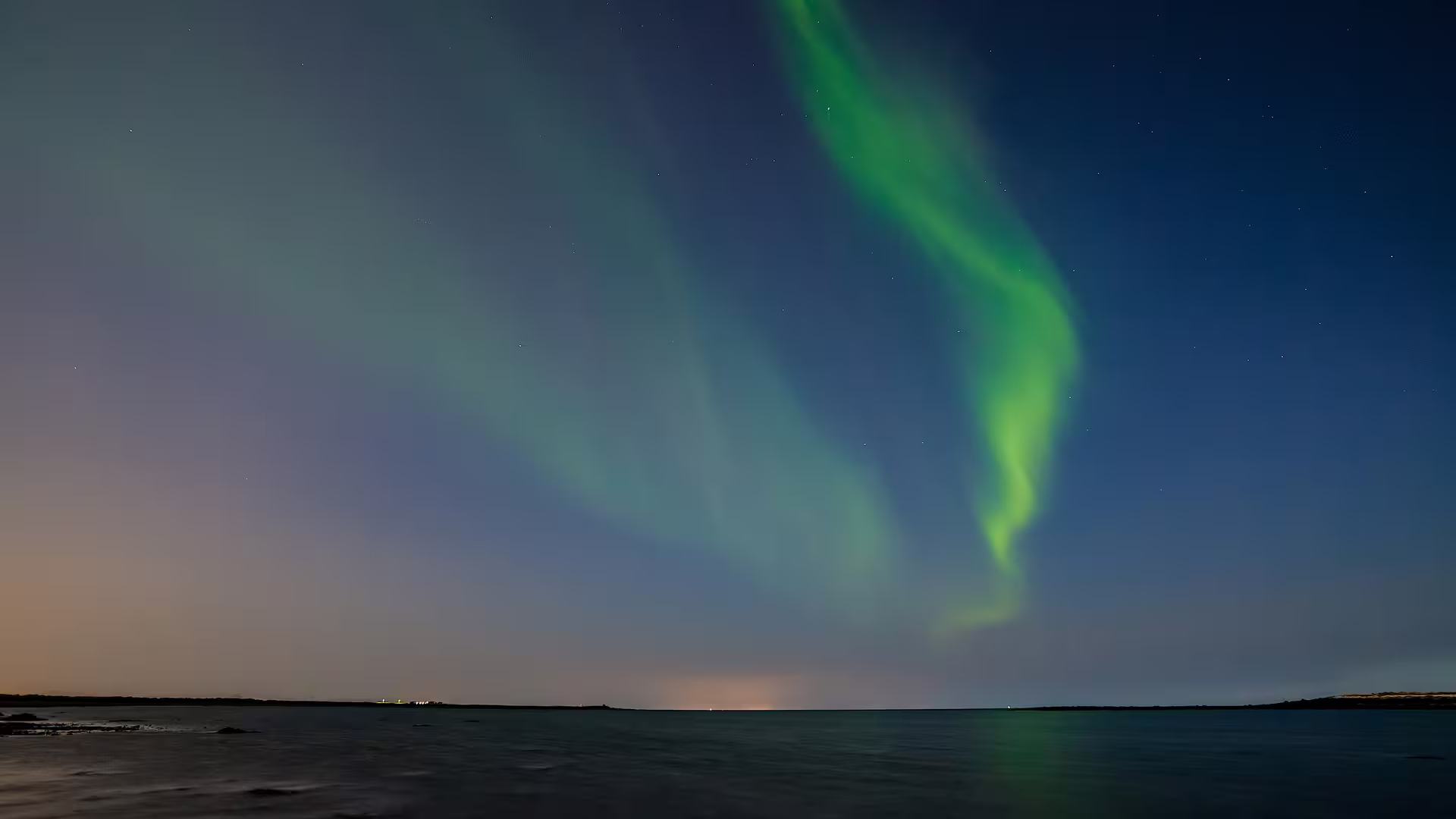 Vivid green aurora borealis dancing over calm ocean waters near Reykjavik Iceland at night