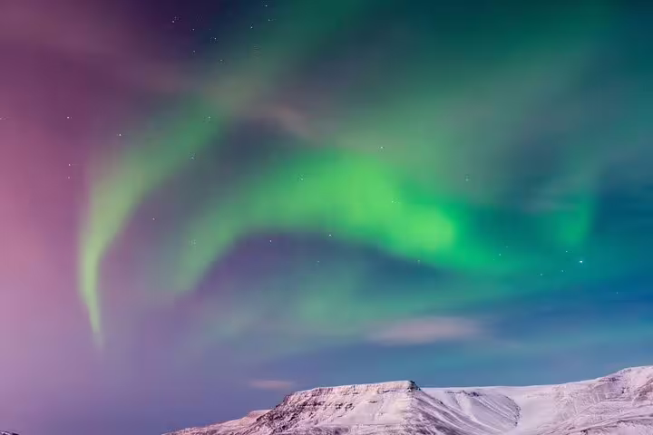 Vivid green and purple aurora borealis swirling over snow-capped mountains in Iceland at night