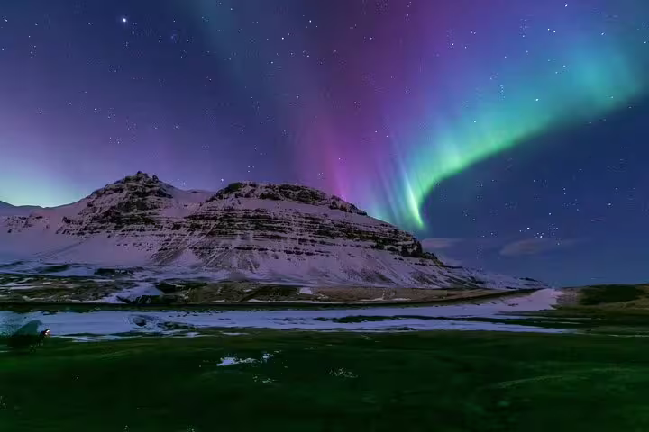 Aurora borealis with purple and green lights over snow-capped mountain in Iceland night sky