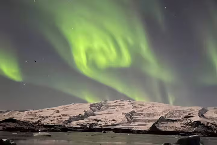 Vivid green aurora borealis swirling over snow-covered mountain landscape at night