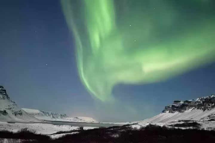 Vivid green aurora borealis swirling over snow-covered mountains at night in Iceland