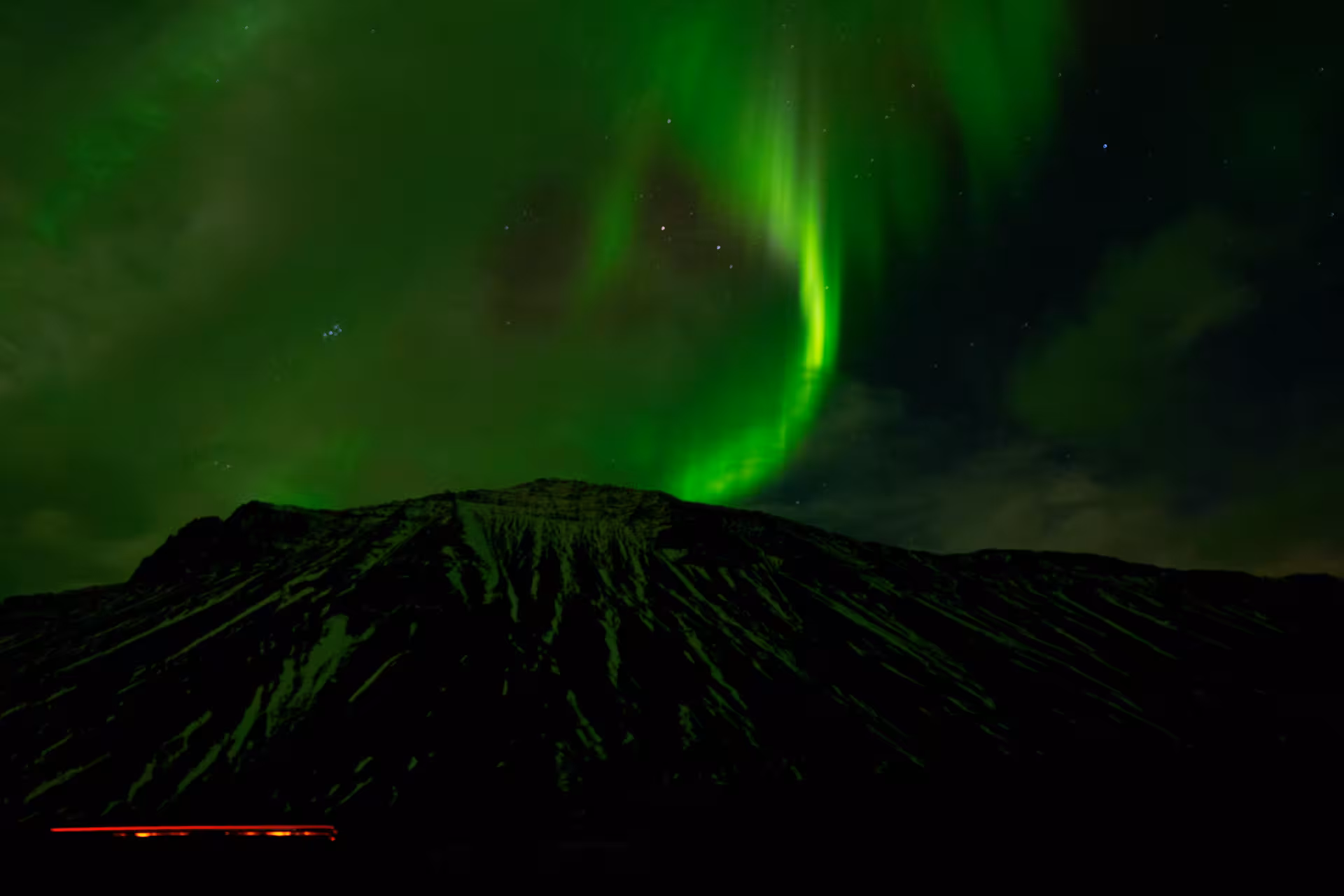 Vivid green northern lights aurora swirling over a volcanic mountain peak on a private 4x4 Iceland tour from Reykjavik