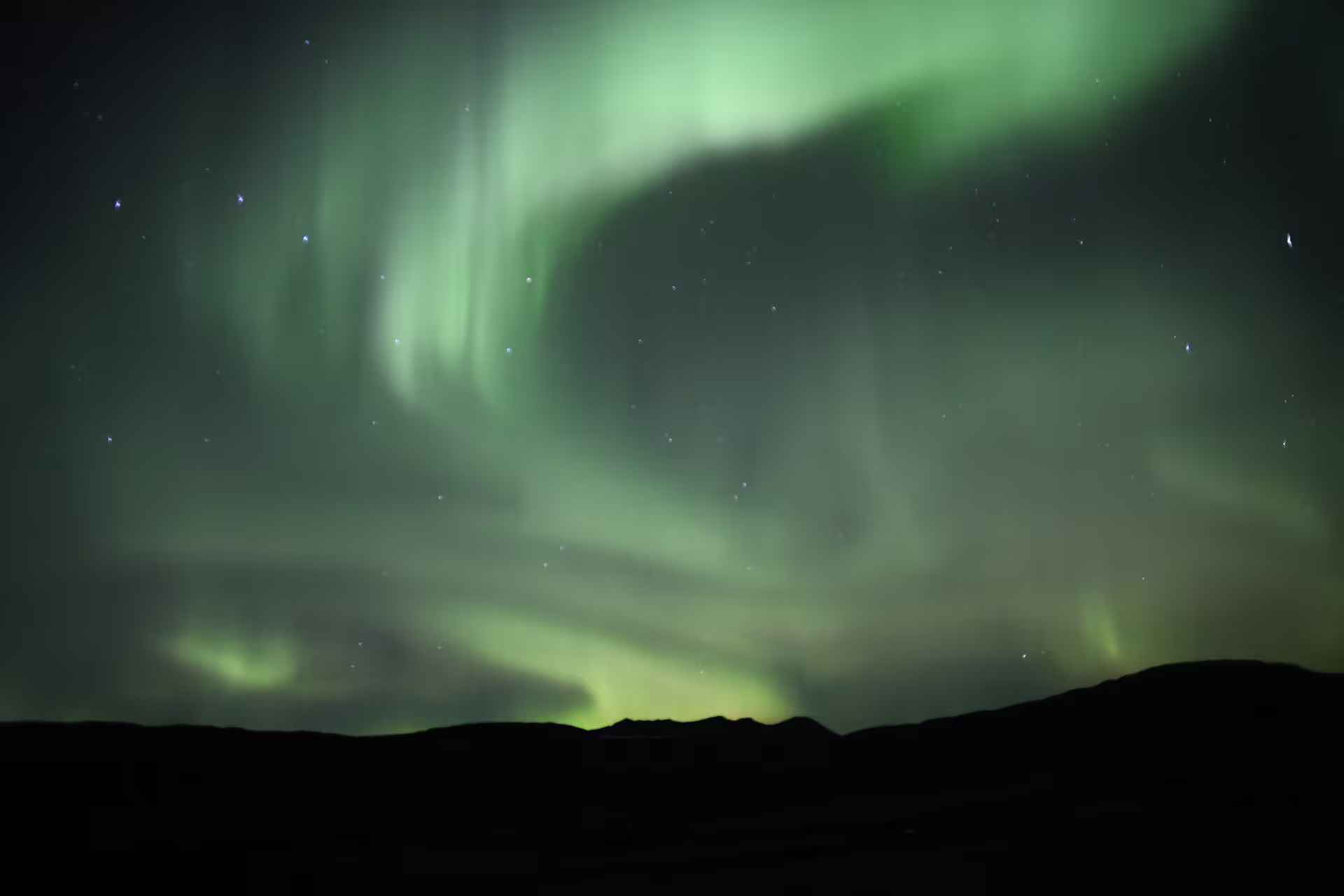 Vivid green northern lights aurora borealis swirling over dark Icelandic mountain silhouette at night