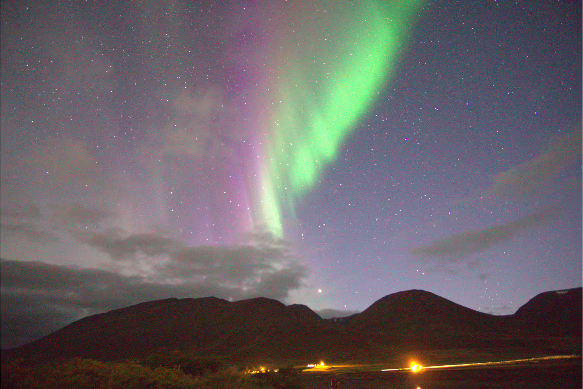 Vibrant green and pink northern lights aurora borealis over dark mountain silhouette in Iceland night sky