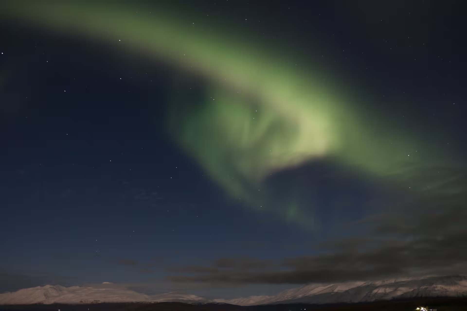 Vivid green aurora borealis swirling over snow-capped mountains in Iceland's night sky
