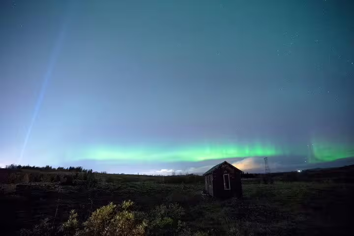 Northern lights aurora borealis glowing green over remote Icelandic landscape with small wooden hut at night