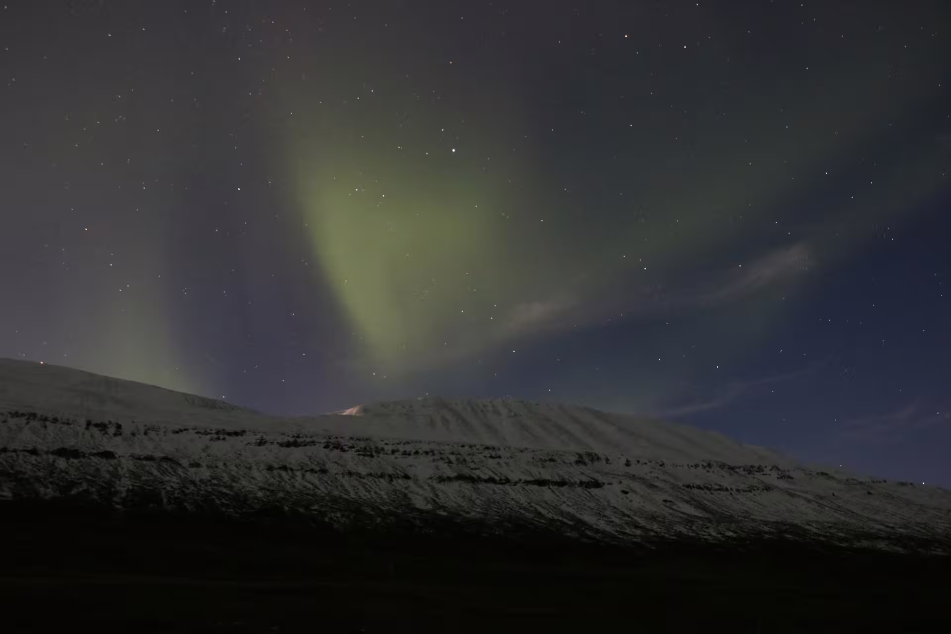 Northern lights aurora borealis glowing green over snow-covered mountain in Iceland at night