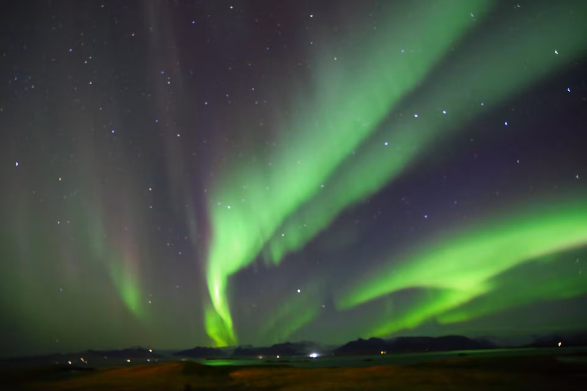 Vivid green northern lights aurora borealis swirling over Iceland's dark landscape and mountains at night