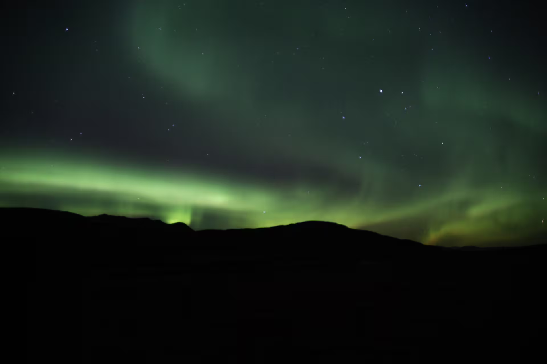 Vibrant green northern lights aurora borealis sweeping over dark mountain silhouettes in Iceland night sky