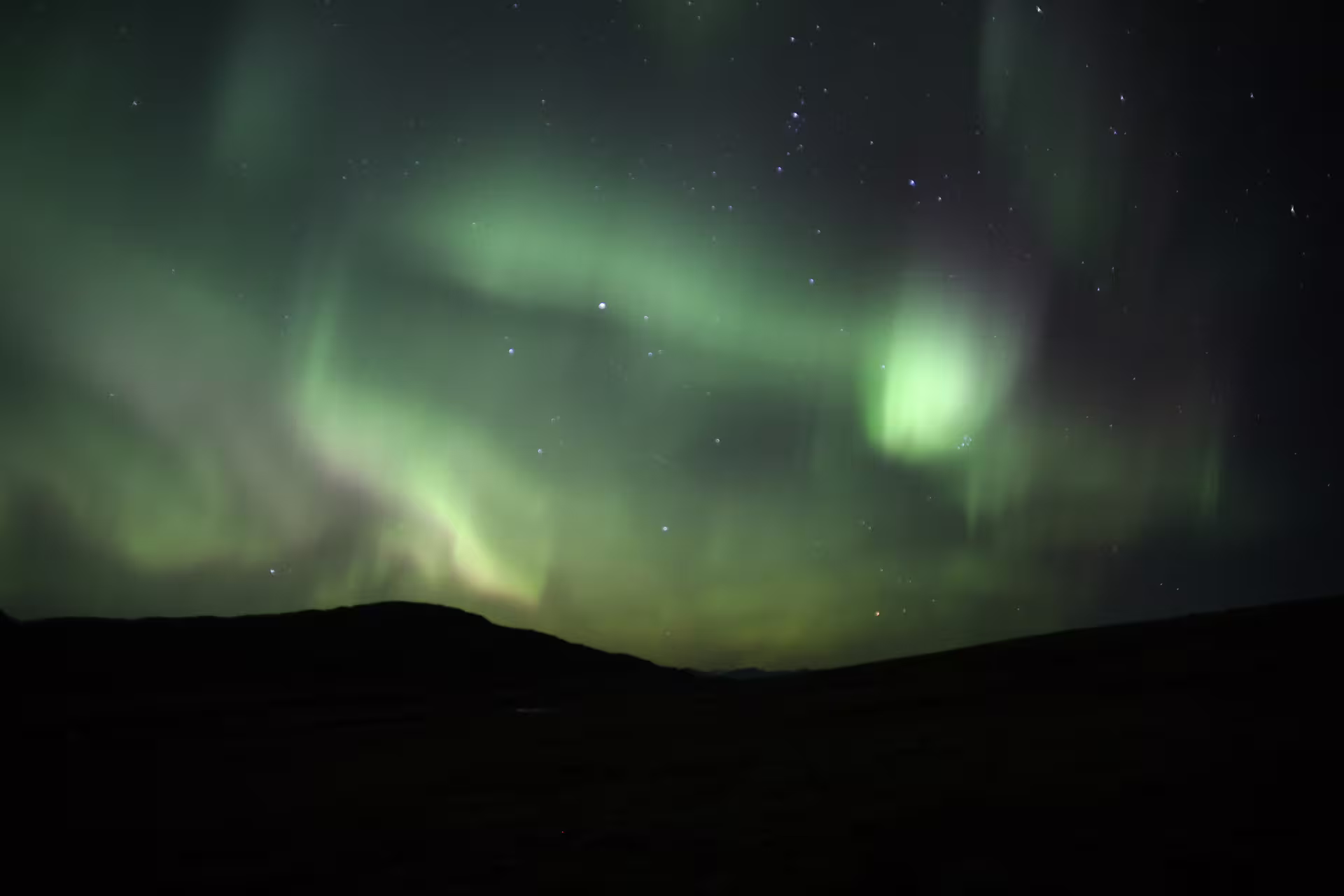 Vibrant green northern lights aurora swirling over dark Icelandic mountain silhouette at night