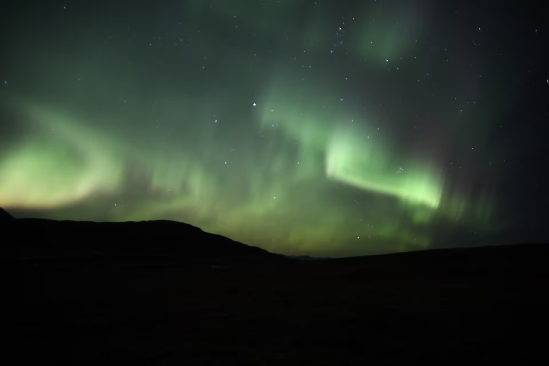 Vivid green northern lights aurora borealis swirling over dark Icelandic highland silhouette at night