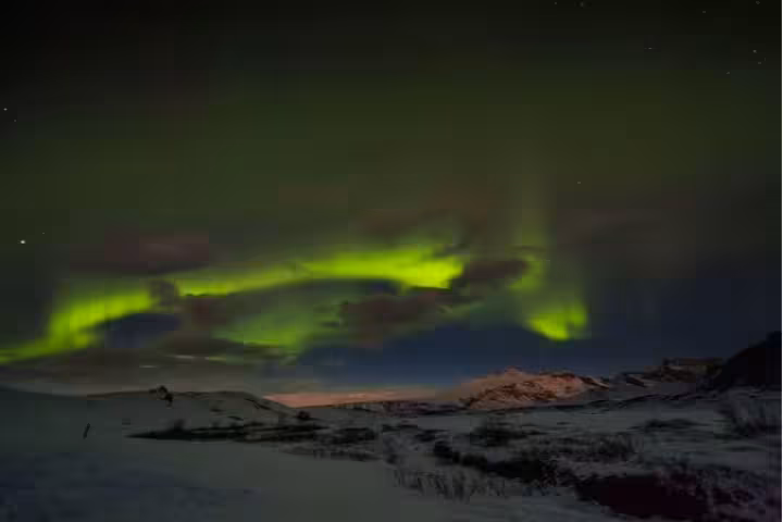 Vivid green northern lights dancing over snow-covered Icelandic landscape at night
