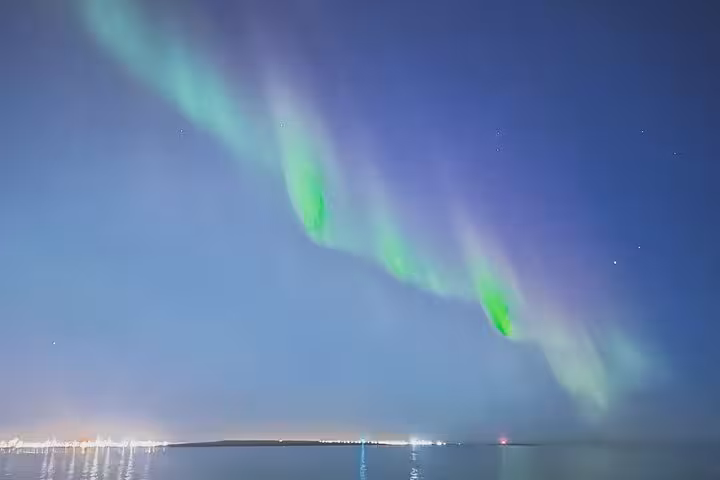 Vivid green and purple northern lights aurora borealis dancing over calm water at night