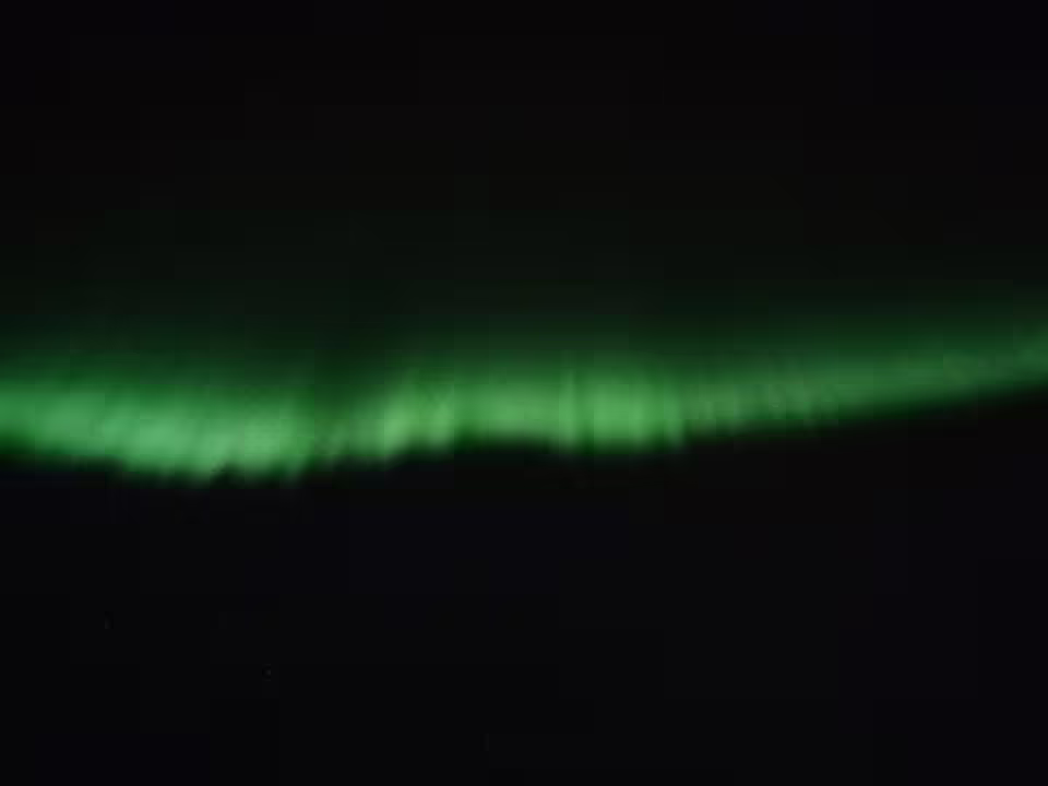 Glowing green northern lights aurora borealis band stretching across dark night sky over Reykjavik Bay